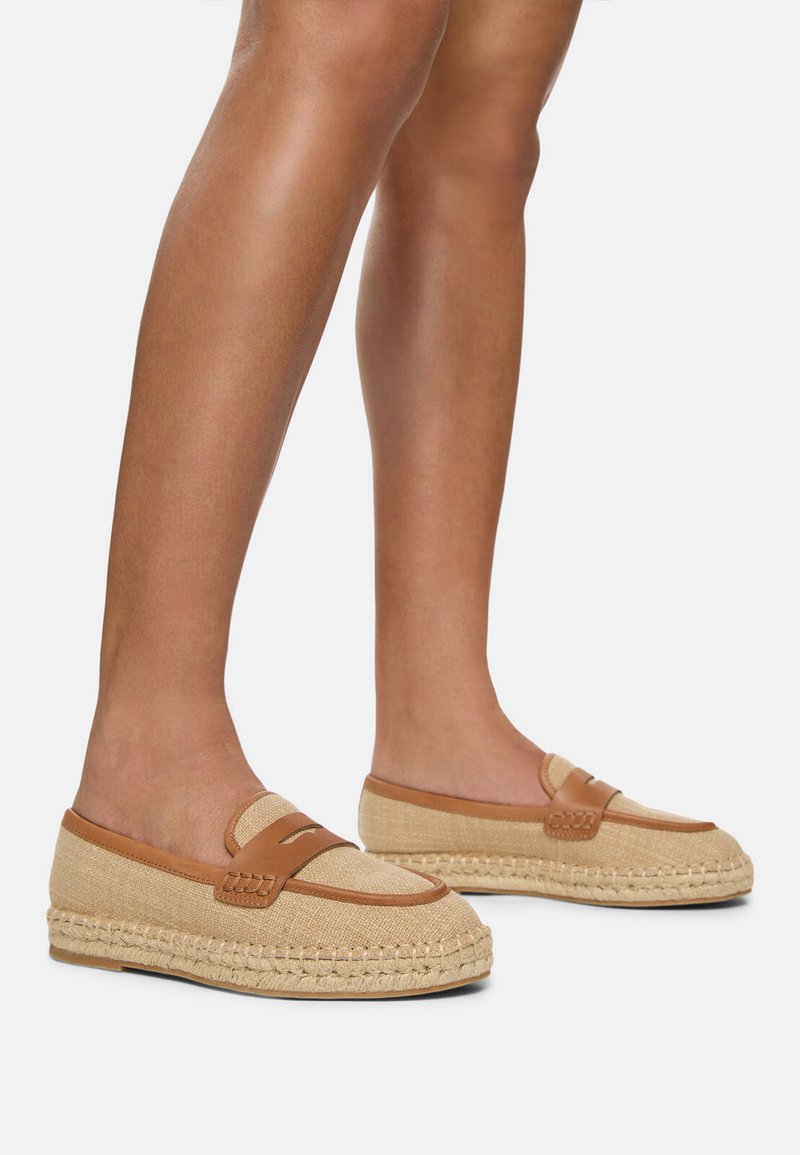 Scarpe slip-on in tela beige con accenti in pelle tan, dotate di una suola in juta intrecciata e un motivo cucito lungo il bordo. Design leggero e casual.