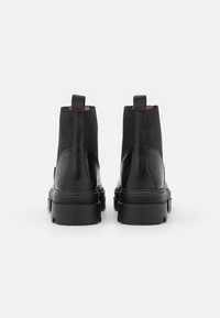Botines de cuero negro hasta el tobillo con paneles laterales elásticos, puntera redondeada, tiradores traseros y suela de goma texturizada. Acabado suave, diseño minimalista.