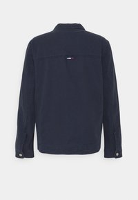 Mörkblå jacka med klassisk krage, långa ärmar, knappmanschetter och en tyglogotypaccents vid axlarna. Mjuk bomullsmaterial.