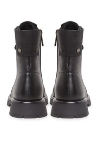 Botas de tobillo de cuero negro con punta redondeada, un acabado texturizado y tachuelas metálicas decorativas en la parte trasera, con una suela de goma gruesa.
