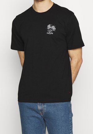 Mand iført en sort Levi's T-shirt med en lille blomster grafik og logo på brystet, kombineret med blå jeans.