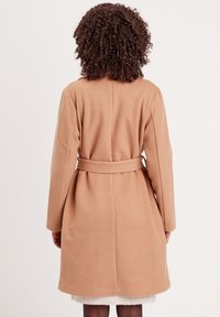 Camel-farbenes Mantel mit tailliertem Schnitt, langen Ärmeln und glatter Textur. Verfügt über ein einfaches Design mit geradem Schnitt und ohne sichtbare Beschläge.