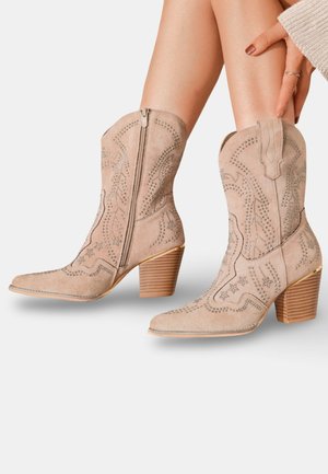 Bottes de cowboy en suède beige avec des orteils pointus, des broderies argentées complexes, une fermeture éclair latérale et des talons en bois empilés.