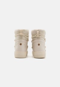 Bottines beiges à la cheville avec une doublure en laine, en cuir texturé, avec un bout rond, un laçage décoratif et un logo circulaire sur le talon.