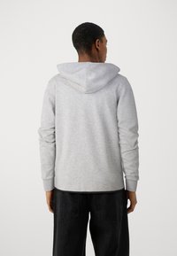 Sudadera gris con capucha ajustable, de mangas largas y puños acanalados. La tela tiene una textura suave y se combina con pantalones oscuros.