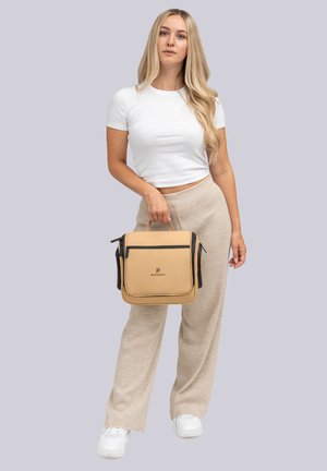 Borsa sintetica beige con manico superiore, tasca frontale con zip e dettagli neri. Indossata da un modello con una camicia bianca e pantaloni beige.