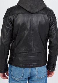 Zwarte leren jas met een gladde textuur, voorzien van een capuchon en gedetailleerde stiksels, gezien vanaf de achterkant met een spijkerbroek.