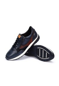 Tummansininen nahkakengät ruskeilla yksityiskohdilla, joissa on nauhat, sivuvetoketju ja valkoinen kumipohja, jossa on kuvioitu pito.