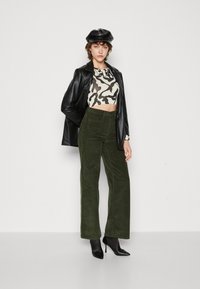 Zwarte leren blazer over een zwart en crèmekleurig camouflage crop top, gecombineerd met groene corduroy wijde broek en zwarte hoge hakken.