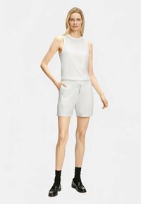 Hellgraues ärmelloses Oberteil und passende Shorts aus glattem Stoff. Die Shorts haben seitliche Taschen. Kombiniert mit schwarzen Socken und Schuhen.