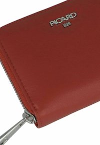 Portefeuille en cuir rouge avec une texture lisse, logo argenté PICARD et fermeture éclair. Présente un détail de couture subtil le long du bord.