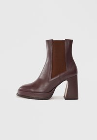 Bottine en cuir bordeaux avec un orteil carré, un insert élastique sur le côté et un talon géométrique épais. Texture lisse avec des accents contrastés.