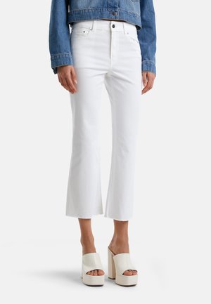 Weiße, kurze Jeans mit ausgefransten Säumen, kombiniert mit cremfarbenen Mules mit Blockabsatz. Gestylt unter einer hellblauen Jeansjacke.