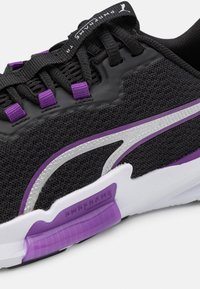 Chaussure de sport noire avec un upper en mesh ornée d'accents violets, de détails argentés et d'une semelle blanche marquée "PWRFRAME".