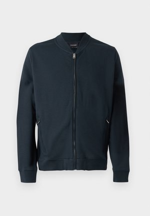 Granatowa kurtka bombowca wykonana z gładkiego materiału, z zamkiem z przodu, bocznymi kieszeniami na zamek błyskawiczny oraz ściągaczami przy mankietach i u dołu.