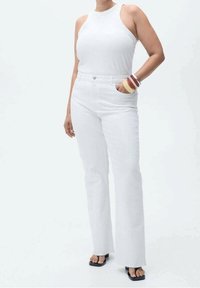 Top blanco sin mangas combinado con jeans acampanados blancos. El conjunto presenta una textura suave y un diseño limpio. Se lleva con sandalias planas negras.