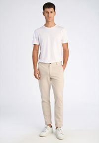 Pantaloni beige a taglio slim con risvolti, abbinati a una t-shirt bianca a girocollo e sneaker bianche. Design semplice, senza fantasie.
