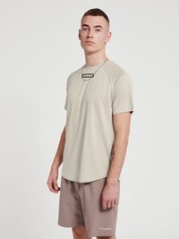 Ljusbeige kortärmad träningsskjorta med rund halsringning och svart logotyp, ihop med taupe shorts. Slät textur, något figurnära design.