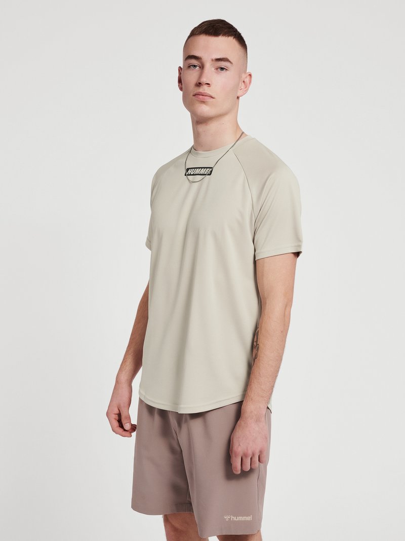 Ljusbeige kortärmad träningsskjorta med rund halsringning och svart logotyp, ihop med taupe shorts. Slät textur, något figurnära design.