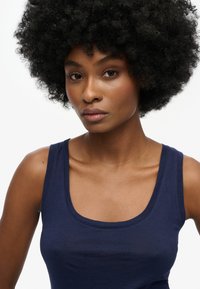 Granatowy bezrękawnik z okrągłym dekoltem, uszyty z miękkiego materiału, o dopasowanym kroju i gładkiej fakturze.