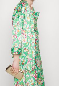 Kwiatowa sukienka w odcieniach zieleni z różowymi, białymi i pomarańczowymi wzorami. Długie rękawy, luźny krój, zestawiona ze złotą kopertówką. Teksturowany materiał.