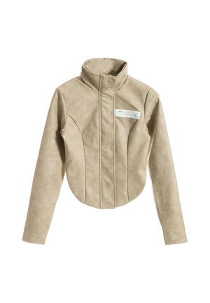 Chaqueta beige de manga larga con cuello alto, costura frontal asimétrica y pequeña etiqueta blanca rectangular en el pecho.
