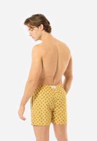 Shorts da bagno gialli con un motivo circolare bianco e rosso, dotati di vita elastica e tasche, visti da dietro.