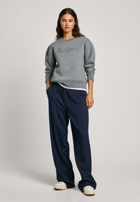 Felpa grigia con "Pepe Jeans" ricamato con fili scuri. Abbinata a pantaloni a gamba larga a righe navy e sneakers bianche.