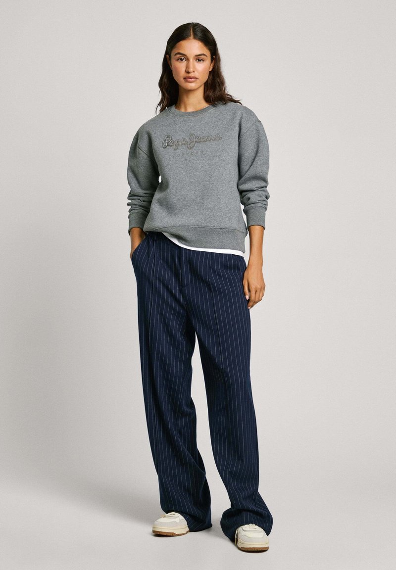 Sudadera gris con "Pepe Jeans" bordado en hilos oscuros. Combinada con pantalones de pierna ancha a rayas en color marino y zapatillas blancas.