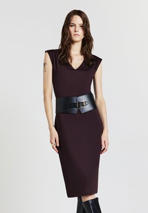 Bodycon-Kleid aus dunkelburgunderfarbenem Stoff, V-Ausschnitt, kurze Ärmel und einem breiten schwarzen Ledergürtel mit einer goldenen Schnalle, kombiniert mit knielangen schwarzen Stiefeln.
