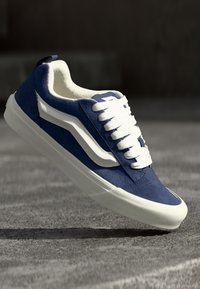 Baskets en daim bleu avec des accents blancs, semelle en caoutchouc plate et lacets blancs. Présentent un bout arrondi et un détail de logo sur le côté.