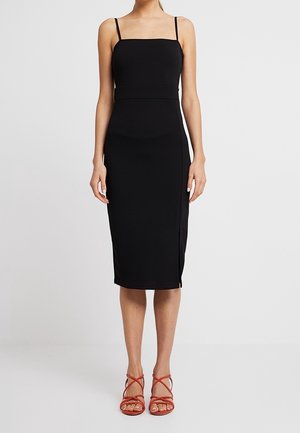 Robe midi noire moulante avec fines bretelles, fente latérale et texture lisse. Assortie à des sandales rouges à lanières.