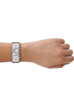 Silberne rechteckige Uhr mit einem Metallarmband am Handgelenk. Die Uhr hat ein weißes Zifferblatt, eine glatte Textur und eine auffällige 'DIESEL'-Markierung.