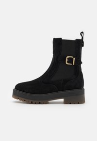 Bottines noires avec un dessus en daim, des panneaux latéraux élastiques, un détail de boucle dorée et une semelle en caoutchouc épaisse à crans pour une meilleure adhérence.
