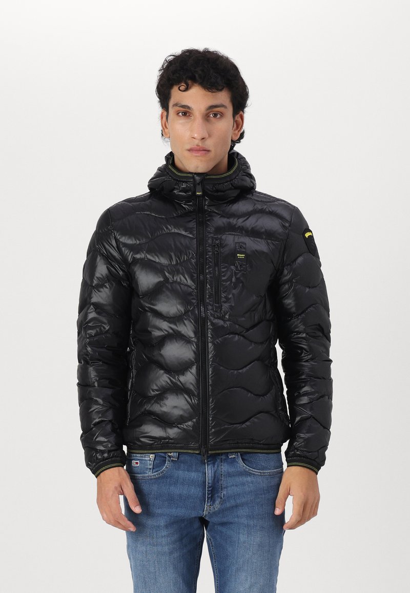 Giubbotto invernale nero con design trapuntato, cappuccio e chiusura con zip. Presenta una tasca sul petto e dettagli verdi lungo il colletto e i polsini.