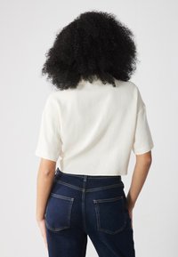 Haut cropped blanc à manches courtes, en tissu texturé, associé à un jean bleu foncé taille haute avec des coutures visibles et des poches arrière.