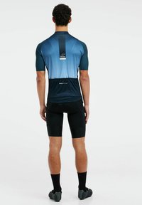 Jersey de ciclismo de manga corta en un degradado azul con tejido texturizado en los hombros, combinado con pantalones cortos negros y zapatos de ciclismo, diseño minimalista.