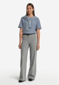 Ljusblå topp med korta ärmar och en matchande tröja knuten över axlarna, tillsammans med grå, vida byxor med smalrand och svarta skor.