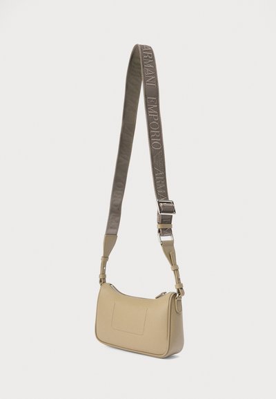 Μπεζ δερμάτινη τσάντα χειρός με λεία υφή, καμπυλωτό σώμα και αποσπώμενο ιμάντα ώμου με γκρι λογότυπο. Απλός σχεδιασμός με μπροστινή τσέπη.