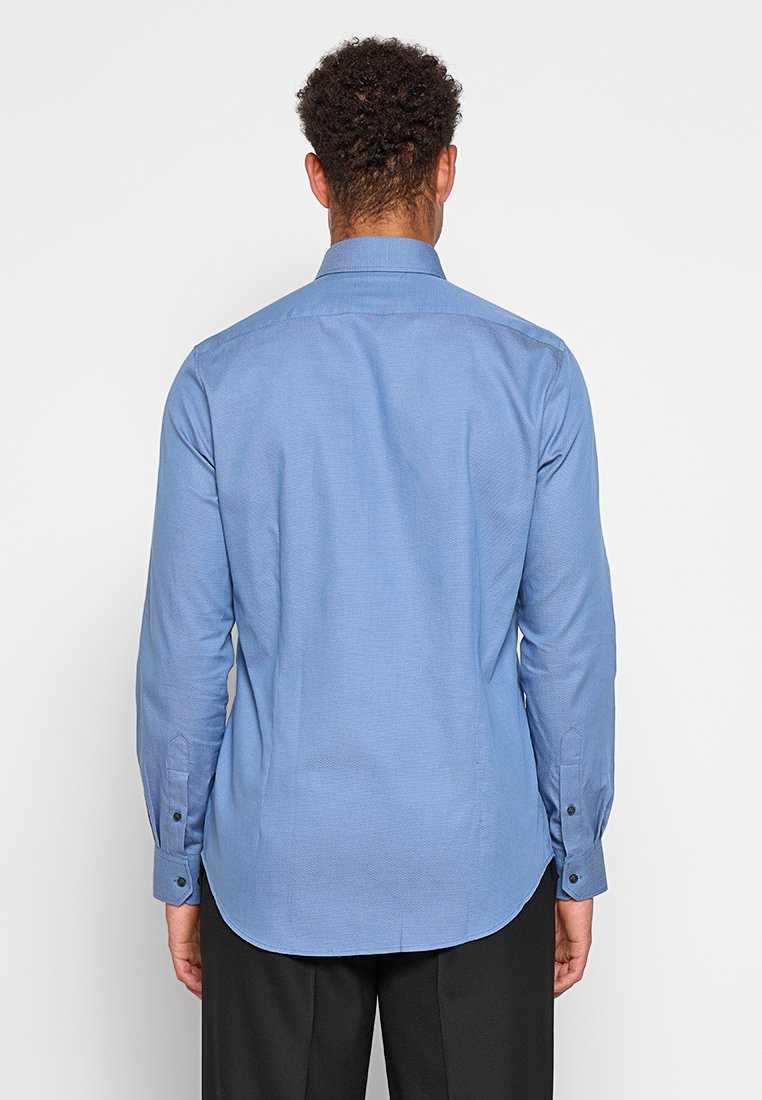 Chemise col bleu clair avec un motif texturé, poignets boutonnés et ourlet arrondi ; fabriquée en tissu tissé. La vue de dos montre une coupe ajustée.