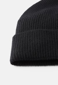 Gorro de malha canelada preto com detalhe de dobra numa fundo branco.