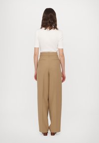 Pantalons beiges taille haute avec une coupe large, tissu texturé, et deux poches arrière. Associés à un simple haut blanc à manches courtes.