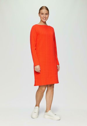 Red knee-length dress with textured zigzag pattern, long sleeves, side slits, paired with white platform sneakers.
