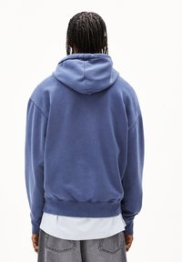 Sweat à capuche en coton bleu clair, présentant une coupe décontractée, des bords-côtes aux poignets et à l'ourlet, avec une poche kangourou et une texture douce.