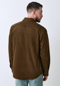 Brown corduroy shirt with long sleeves, button cuffs, and a flat collar. Features a texture typical of corduroy fabric.