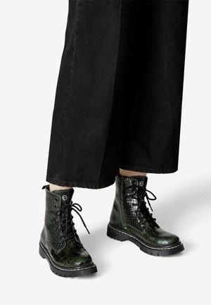 Botas de combate negras con un patrón de cocodrilo brillante, diseño con cordones y suela gruesa. Las botas tienen costuras y ojales en contraste.
