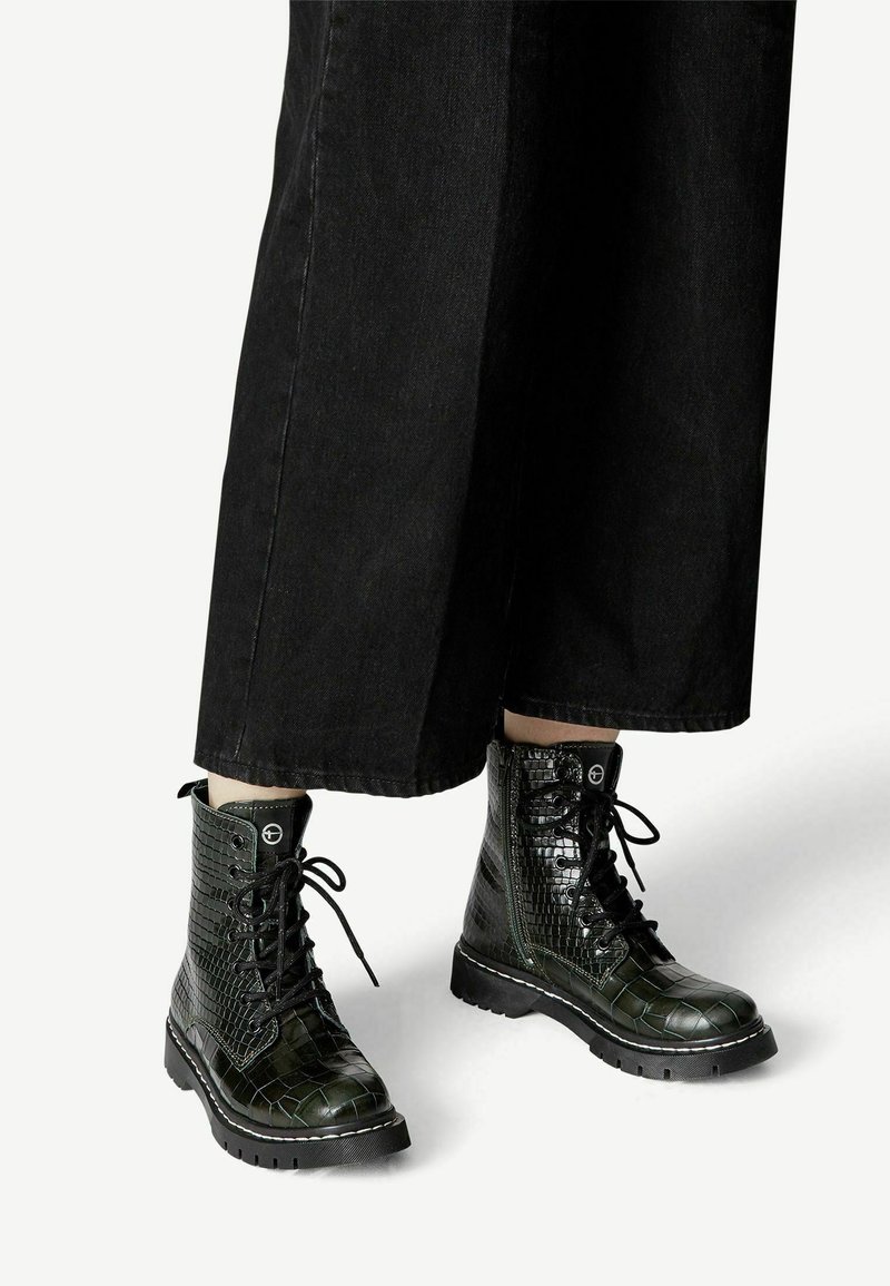 Zwarte combatboots met een glanzend krokodillenpatroon, vetersluiting en een stevige zool. De boots hebben contrasterende stiksels en veterogen.
