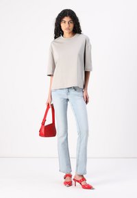 Grå t-skjorte med korte ermer, lyseblå jeans, rød håndveske og røde spisse høye hæler med metalliske detaljer. Enkel design med en avslappet passform.
