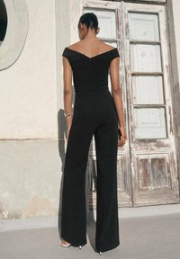 Schwarzer Off-Shoulder-Jumpsuit mit tailliertem Oberteil und weit geschnittenen Hosenbeinen, mit einem Reißverschluss hinten und glatter Textur.