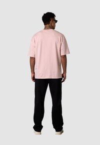 Light pink oversized t-shirt with short sleeves, paired with black pants. The fabric appears soft, and the fit is relaxed.